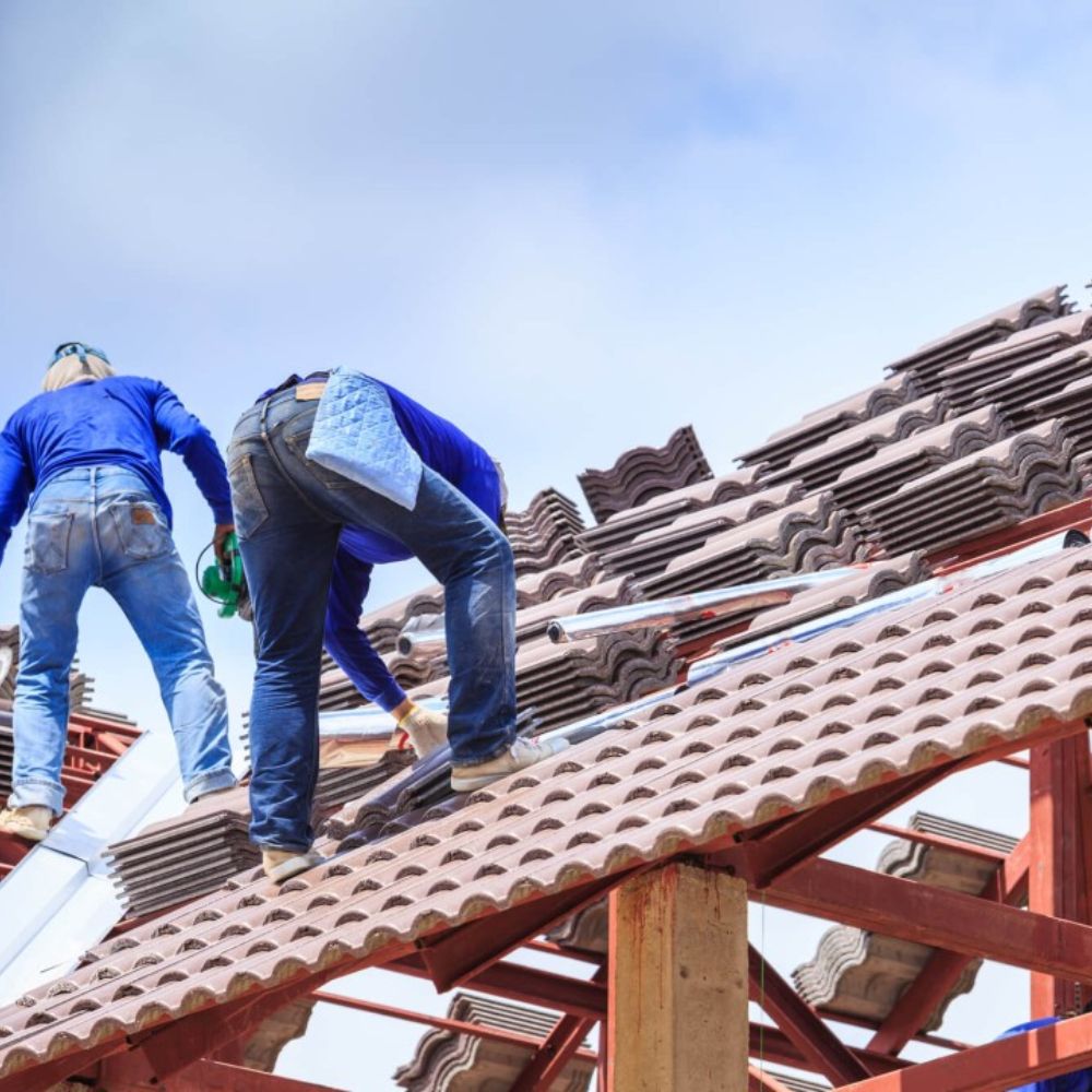 Two workers engaged in roofing tasks against a bright blue sky, representing a roofing service in Sacramento, CA.