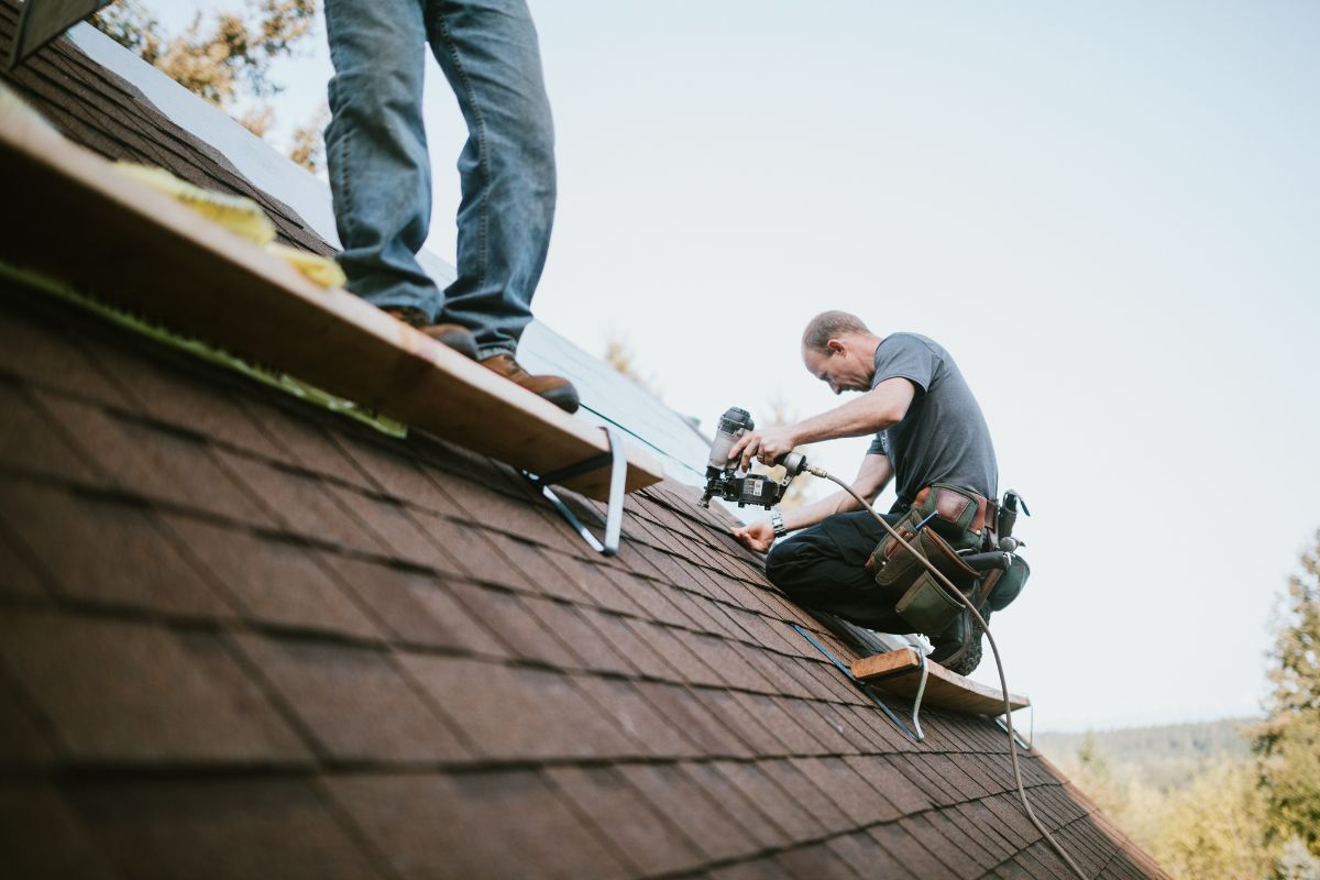 Two men collaborating on a rooftop, engaged in construction work under clear skies.