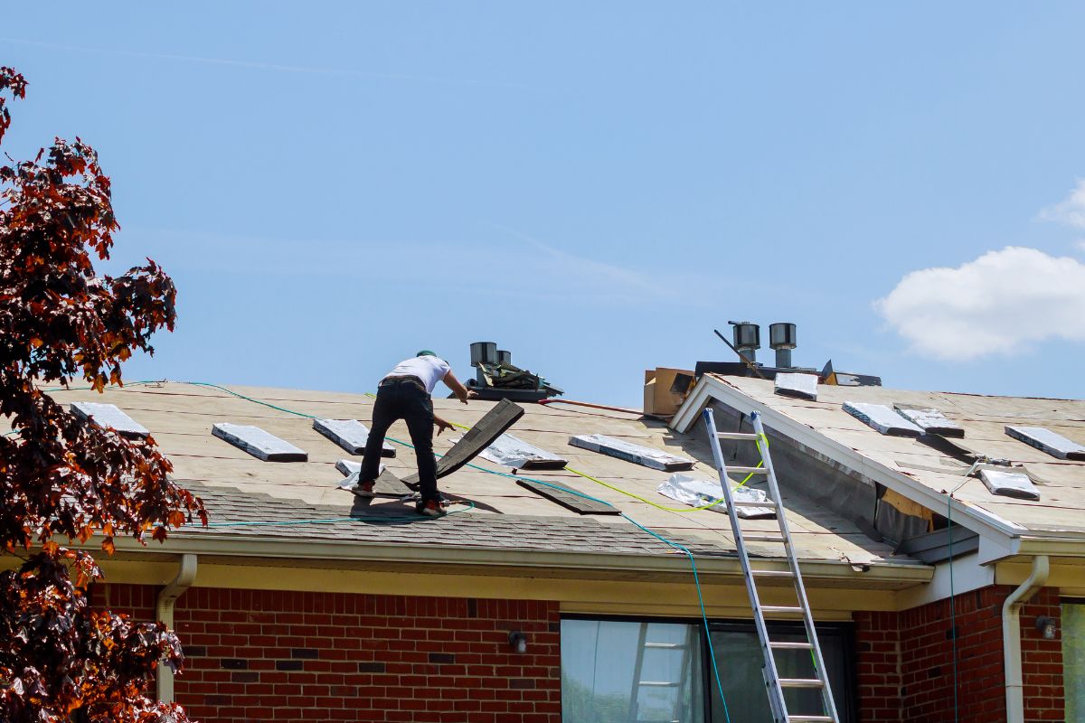 A man is diligently working on the roof of a house, focused on his task amidst a clear blue sky.