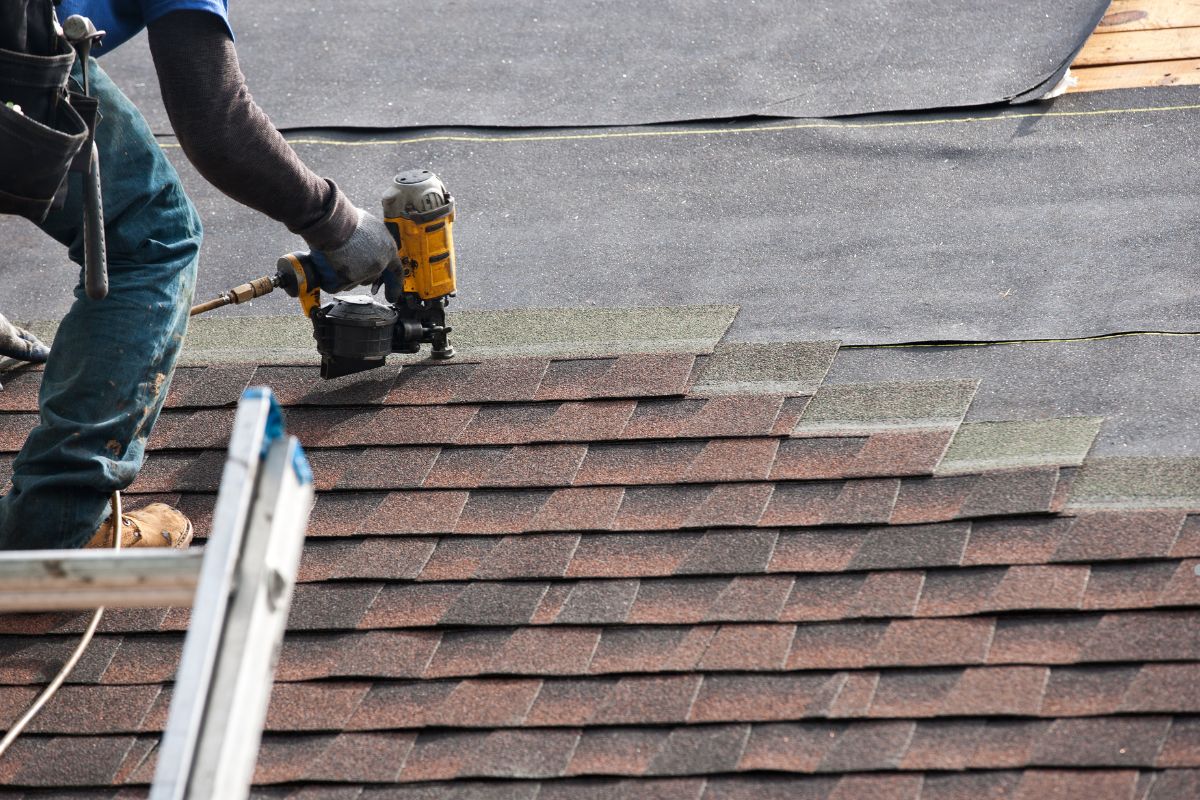  A man using a nail gun to work on a hip and gable roof, focused on repairing the structure.