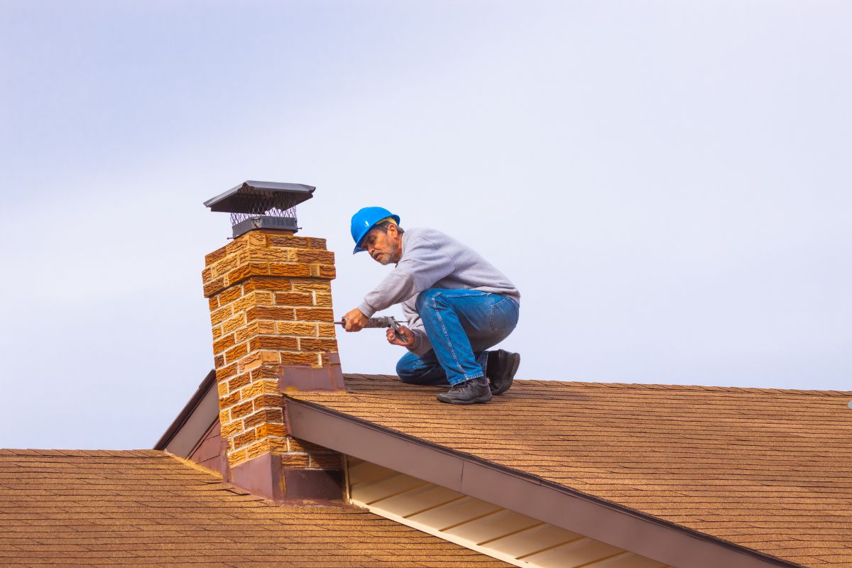 A man, identified as a reputable roofing contractor, is working on the roof of a house, focused on his task. 