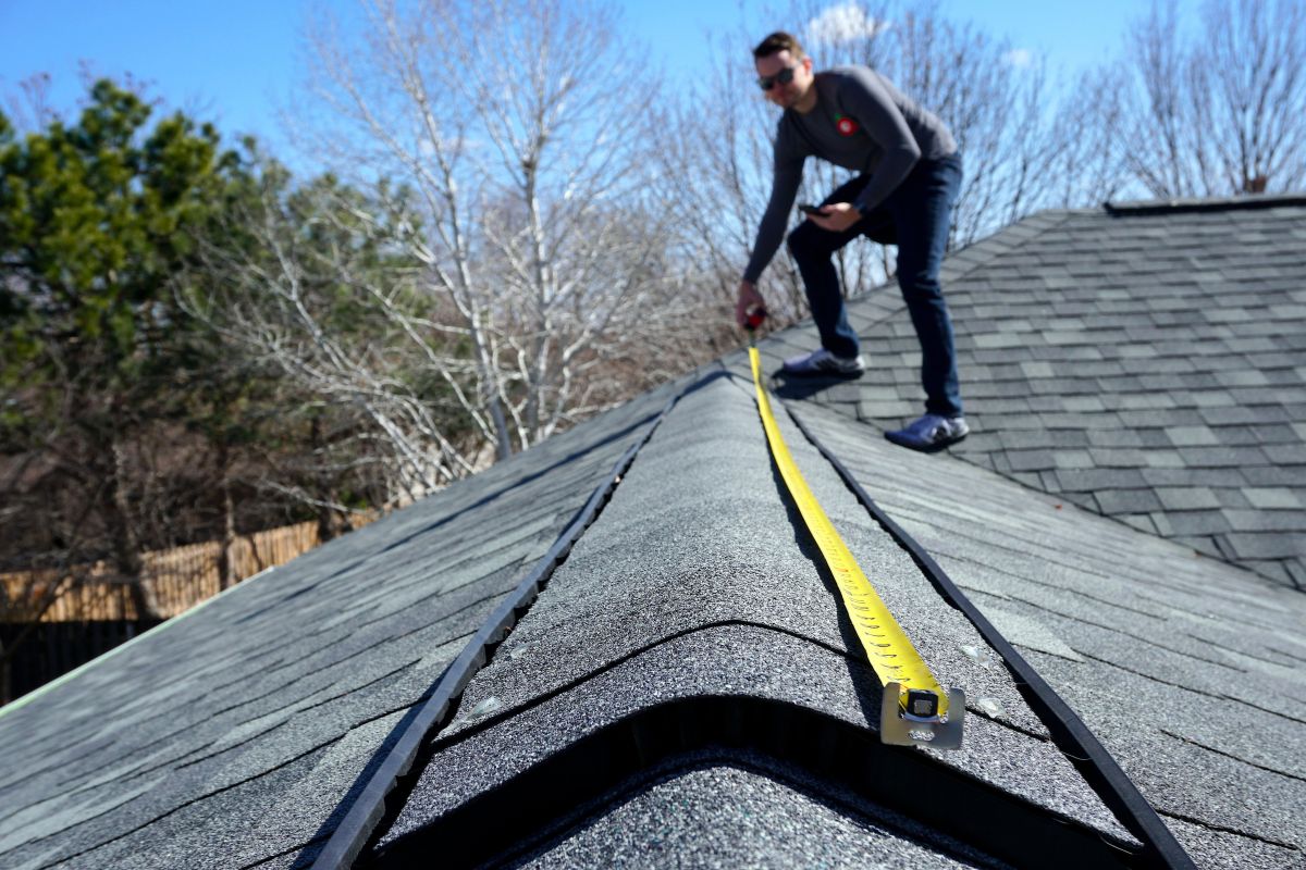 A man measuring the roof of a house in preparation for a roof replacement project.